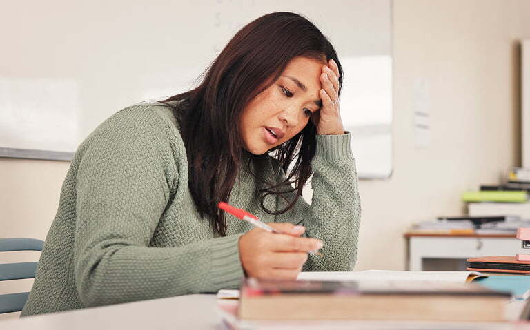 Female Asian BCBA stressed with workload while writing notes in office